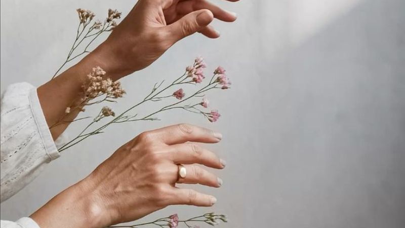 Mãos femininas com flores secas expressam o processo natural de envelhecer com dignidade.